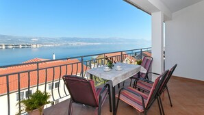 Un balcone con tavolo e sedie, vista su uno specchio d'acqua e una città in lontananza.