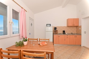 A compact kitchen with a microwave, coffee maker, and a small refrigerator. There is a dining table with chairs and a potted plant.
