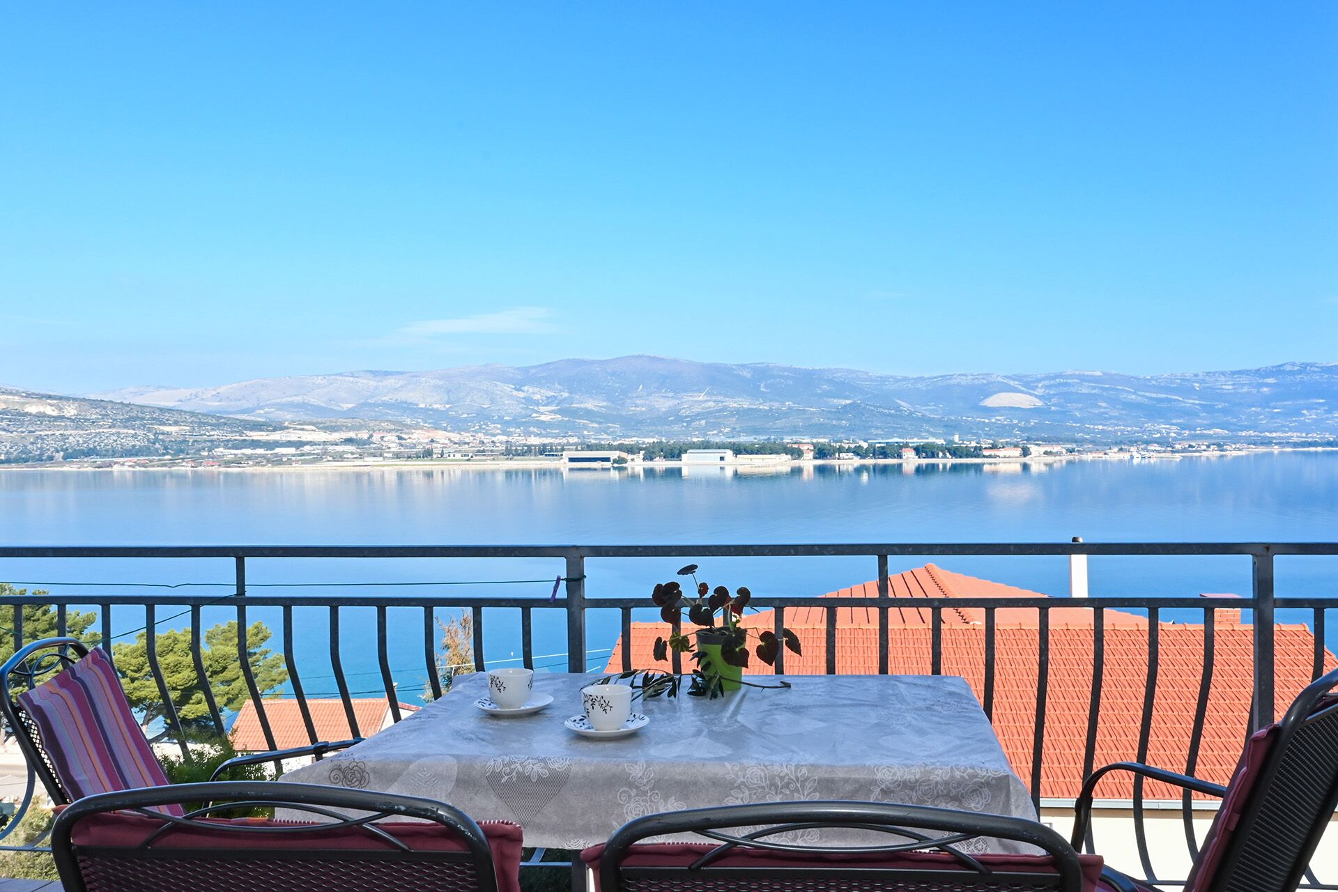 A terrace with a table set for two, overlooking a calm lake and distant mountains.
