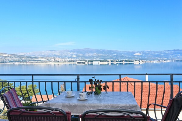 Une terrasse avec une table dressée pour deux personnes, offrant une vue sur un lac paisible et des montagnes lointaines.