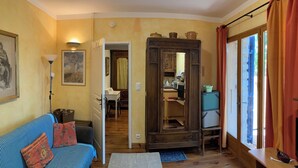 A cozy living room with a sofa, a coffee table, and a wooden cabinet. A kitchen is visible through an open doorway.