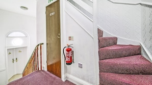 En trappe med rødt mønstret tæppe, en trædør med teksten "Fire Exit", og en brandslukker ophængt på væggen.