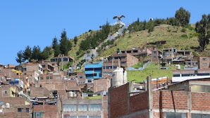 A densely packed hillside residential area with multi-story brick buildings, some with blue roofs, and a clear blue sky above.