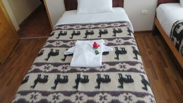 Una cama bien hecha con un edredón estampado, una almohada blanca y una toalla blanca doblada con una rosa roja.