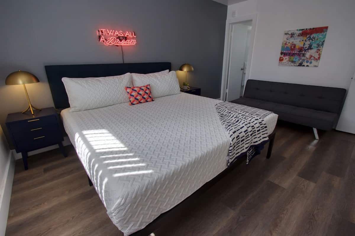 A neatly arranged bedroom with a bed, bedside tables, a bench, and a neon sign.