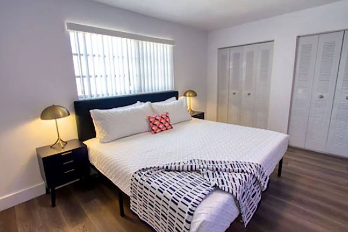 A bedroom with a bed, two bedside tables, a window with blinds, and a wardrobe.