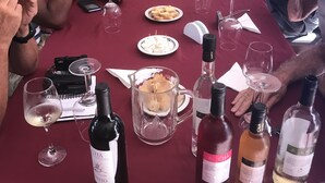 Un groupe de personnes est assis autour d’une longue table, devant des bouteilles de vin et des verres.