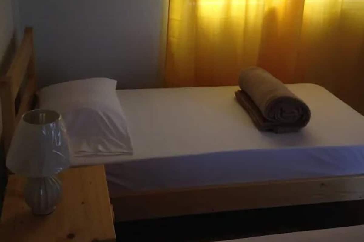 Un lit simple avec un drap blanc, une serviette enroulée et un verre posé sur une table de chevet en bois.