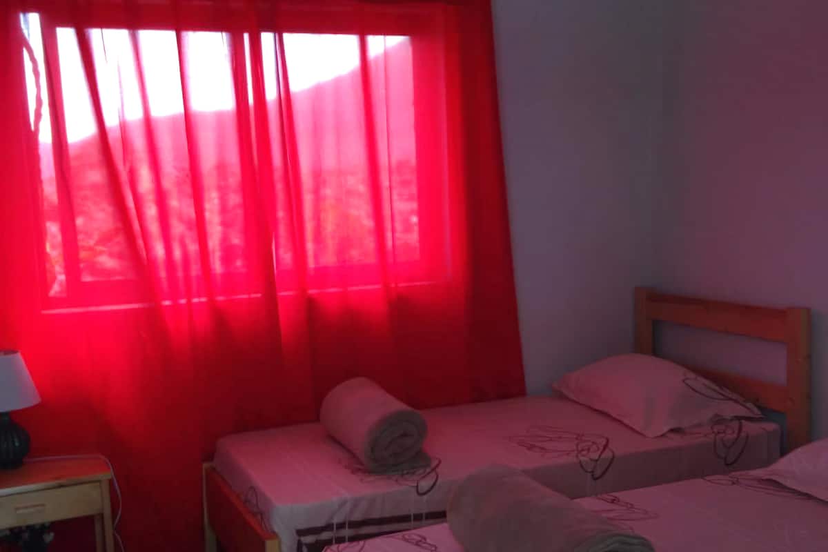 Une chambre avec deux lits simples, une petite table avec une lampe et des rideaux rouges.