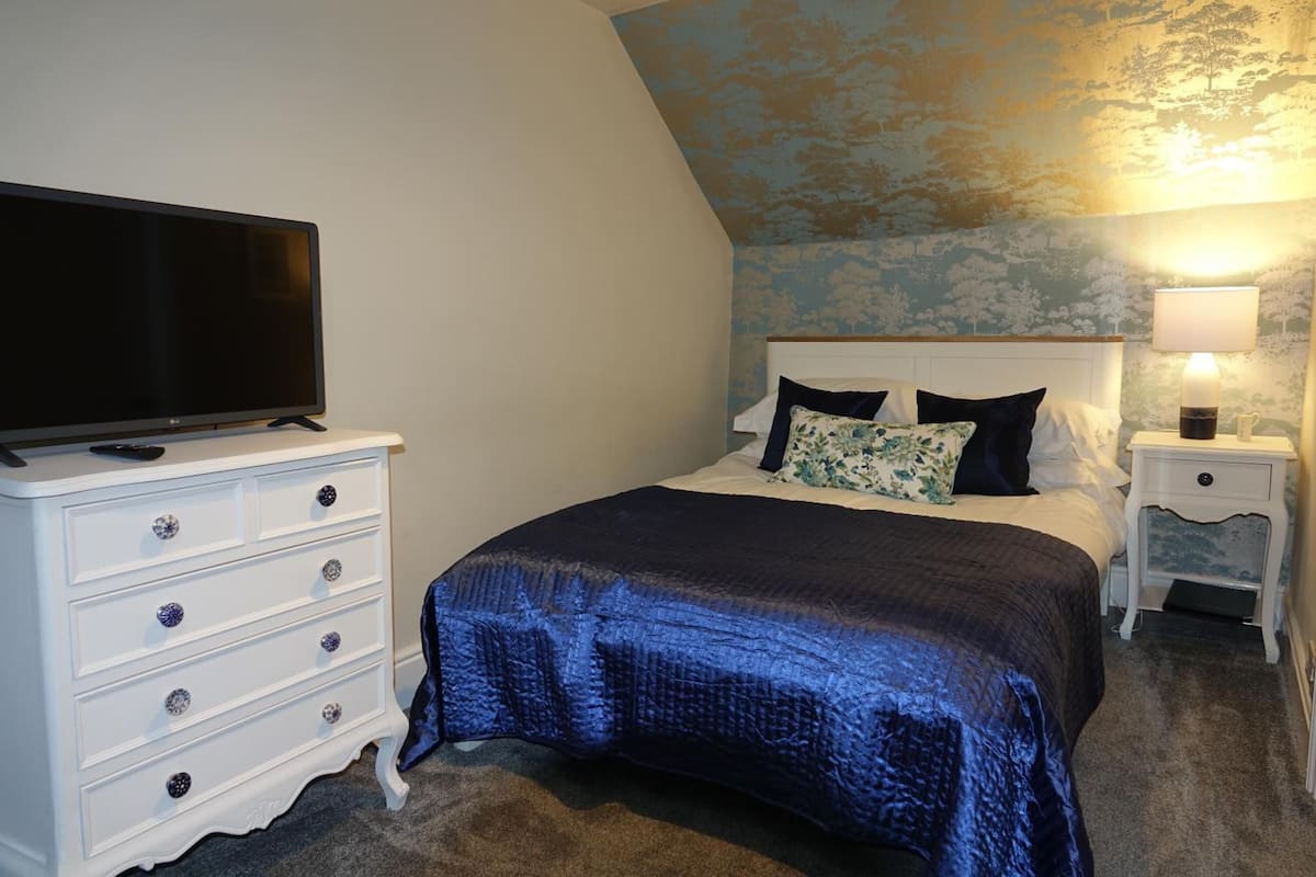 A bedroom with a bed, a dresser, a nightstand, a lamp, and a television.