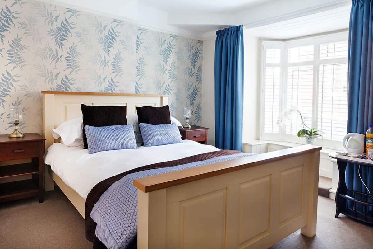 A neatly made bed with a wooden headboard, a bedside table with a lamp, and a window with blue curtains.
