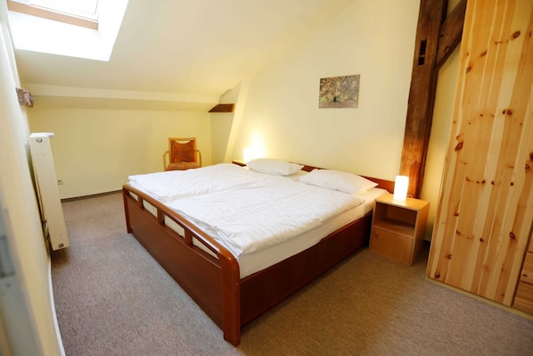 Une chambre avec un lit en bois, une table de chevet, une chaise et une armoire en bois.