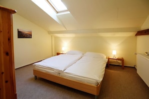 Ein Schlafzimmer mit Oberlicht, einem Bett mit weißen Leinentüchern, zwei Nachttischen mit Lampen und einem kleinen Gemälde an der Wand.