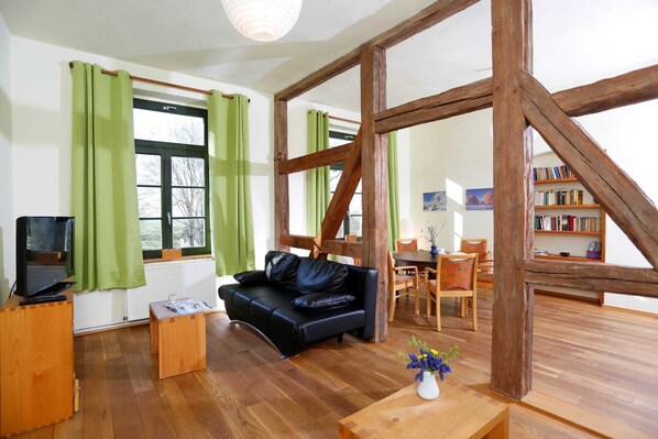 Una habitación con suelo de madera, un sofá de cuero negro, una mesa de centro de madera, un televisor y una estantería.