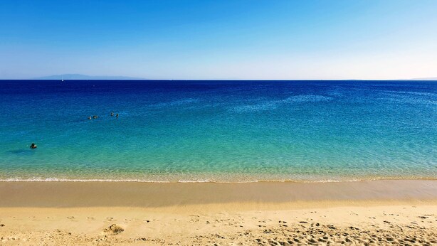 Une plage avec une eau d’un bleu limpide et un rivage sablonneux.
