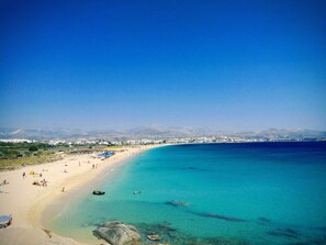 Une plage aux eaux turquoise et limpides, un rivage sablonneux et une vue lointaine sur la ville.