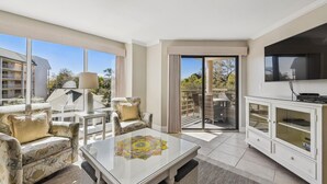 A spacious living area with a glass-top coffee table, wicker furniture, and a television mounted on the wall.