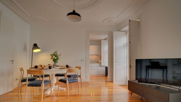 A modern living room with a wooden floor, a dining area with a table and chairs, a TV on a stand, and a pendant light. - Tracey & Neill's Place by Portugal Portfolio (Misericórdia/ Lisbon)