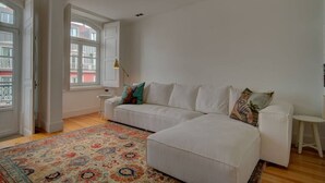 A spacious living room with a white sofa, a patterned rug, and a view through a large window. - Tracey & Neill's Place by Portugal Portfolio (Misericórdia/ Lisbon)