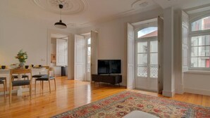 A spacious living room with a large TV, a dining area with chairs, and a colorful rug. - Tracey & Neill's Place by Portugal Portfolio (Misericórdia/ Lisbon)