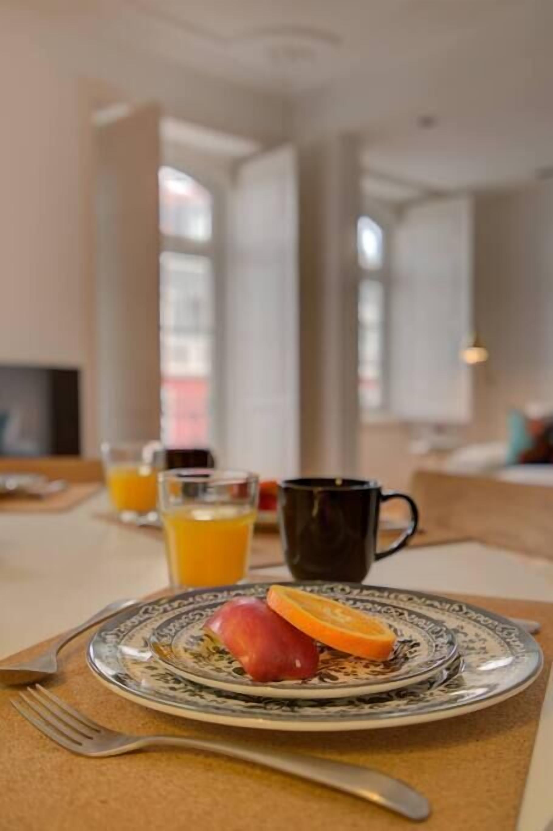 A breakfast setting with a plate of fruit, a cup, and a glass of orange juice on a table.