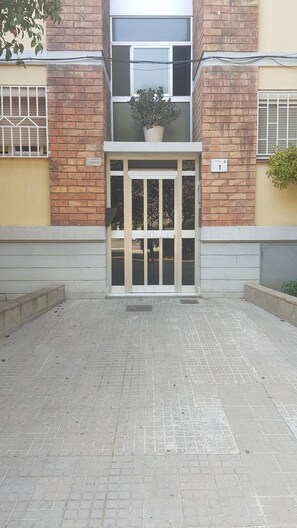 A building entrance with a gated door, a potted plant on the landing, and a brick facade. - Private Rooms - Fira 2 (Sant Boi de Llobregat)