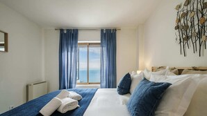 Habitación de hotel con una cama grande, vista al mar por la ventana y una obra de arte en la pared.