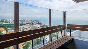 Un balcón con banco de madera, ventanas amplias y vista panorámica de la ciudad.