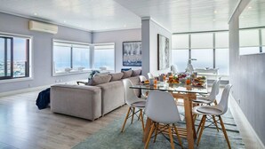 Una sala de estar moderna con una mesa de comedor de vidrio, un sofá gris y grandes ventanales con vistas a la ciudad.