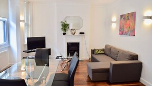 A modern living room with a glass dining table, a sofa, a TV, and a fireplace.