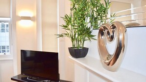A modern living room with a flat-screen TV, a potted bamboo plant, and a heart-shaped decorative item on a white mantelpiece.
