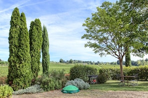 Stroll through the tranquil garden, surrounded by mature trees and neatly trimmed hedges, along a gravel path leading to a serene bench.