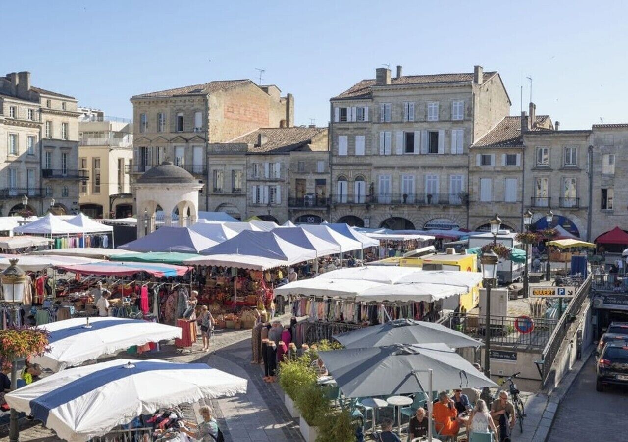 Un marché animé en plein air, avec de nombreux étals abrités sous des auvents blancs, entouré de bâtiments historiques.