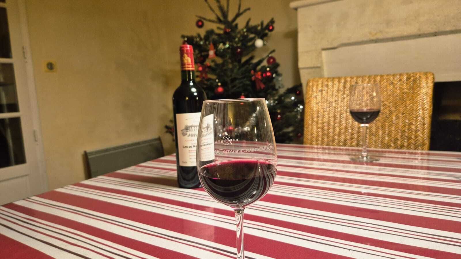 Una mesa con mantel a rayas, una copa de vino tinto y una botella de vino al fondo.