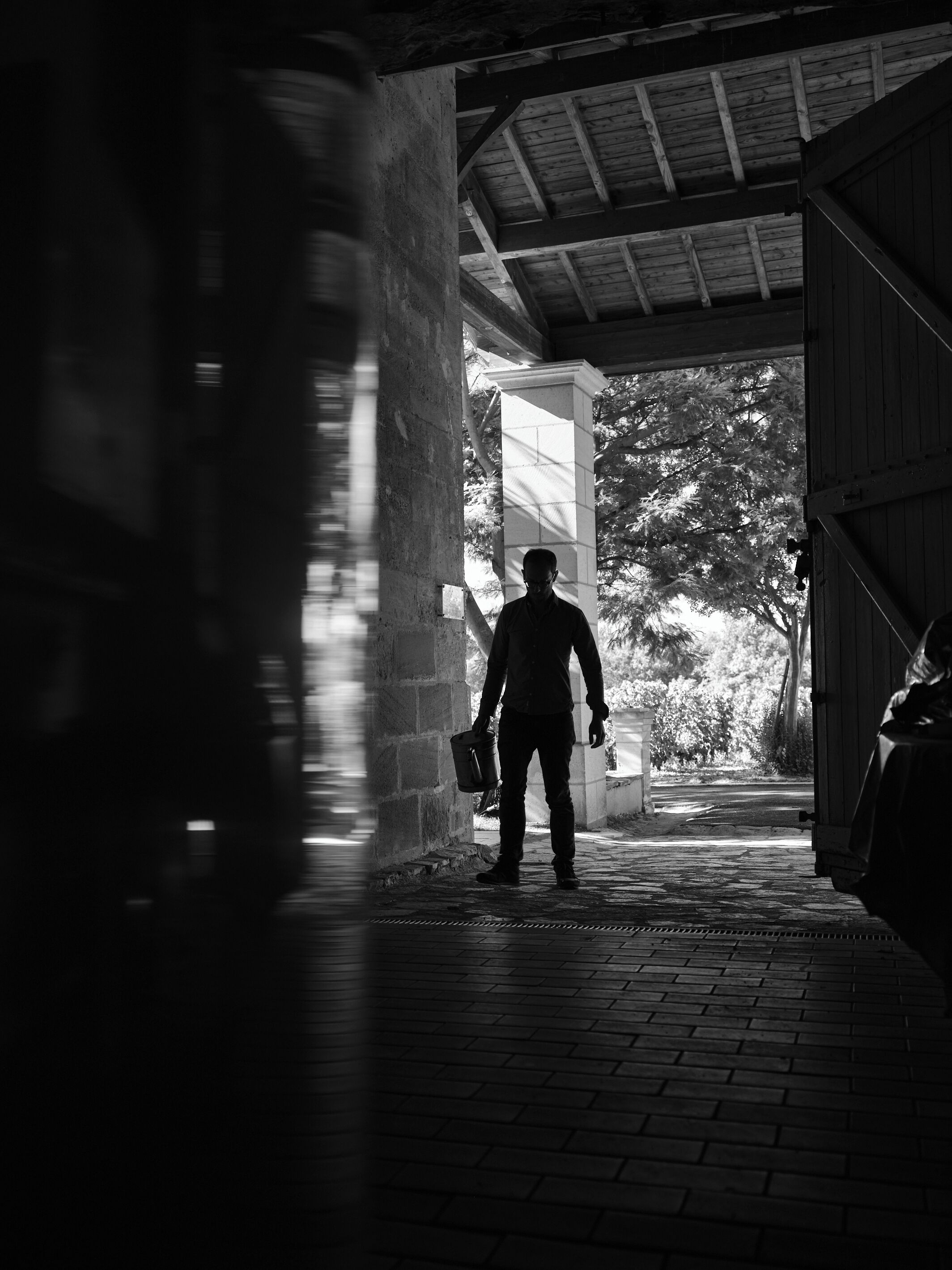 A person walking through a dimly lit brick corridor with a wooden ceiling and columns.