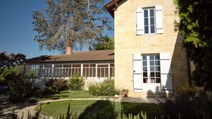 A two-story stone building with a tiled roof, large windows, and shutters. - Renovated Stone House with Garden in the Heart of the Saint-Émilion Vineyards (ST EMILION)
