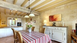 A dining area with a striped tablecloth, wicker chairs, a vase with flowers, and a white cabinet with a lamp. - Renovated Stone House with Garden in the Heart of the Saint-Émilion Vineyards (ST EMILION)