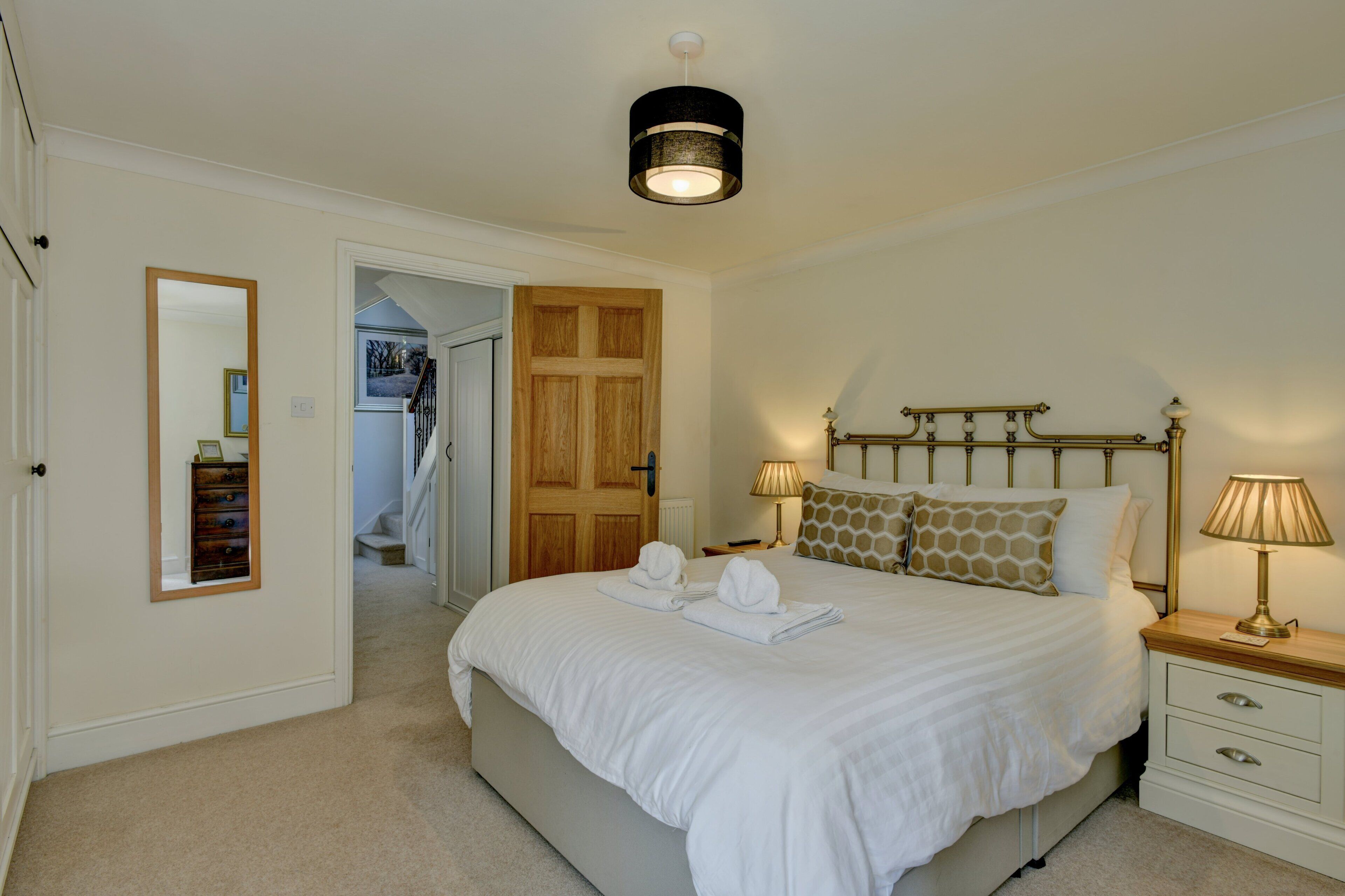 A neatly arranged bedroom with a large bed, bedside lamps, a wooden door, and a mirror on the wall.