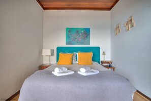 Une chambre d’hôtel avec un lit, deux oreillers, un tableau au mur et une petite table avec une lampe.