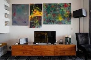 Un salon moderne avec un meuble en bois, un téléviseur à écran plat et des œuvres d’art abstraites accrochées au mur.