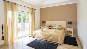 Une chambre à coucher avec un lit, deux tables de chevet, une fenêtre avec des rideaux et une vue sur l’extérieur.