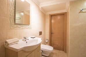 A bathroom with a sink, mirror, toilet, and wooden door. - Villa Hera | 6 Bedrooms | Outdoor Spa & More | ViIamoura (Vilamoura)