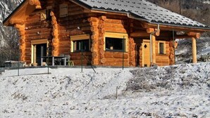 A log cabin with a sloped roof, wooden exterior, and large windows, surrounded by snow-covered mountains and clear skies. - ----The evening Star---- (Saint-Martin-de-la-Porte)
