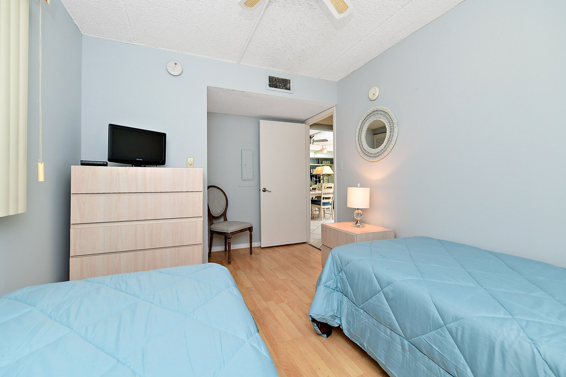 Een slaapkamer met twee bedden, een televisie op een dressoir, een stoel, een spiegel en een deur naar een badkamer.