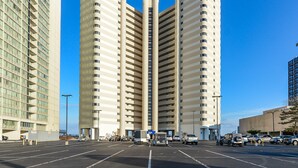 Un edificio de gran altura con un hueco central para ascensores, rodeado por un estacionamiento con varios coches.
