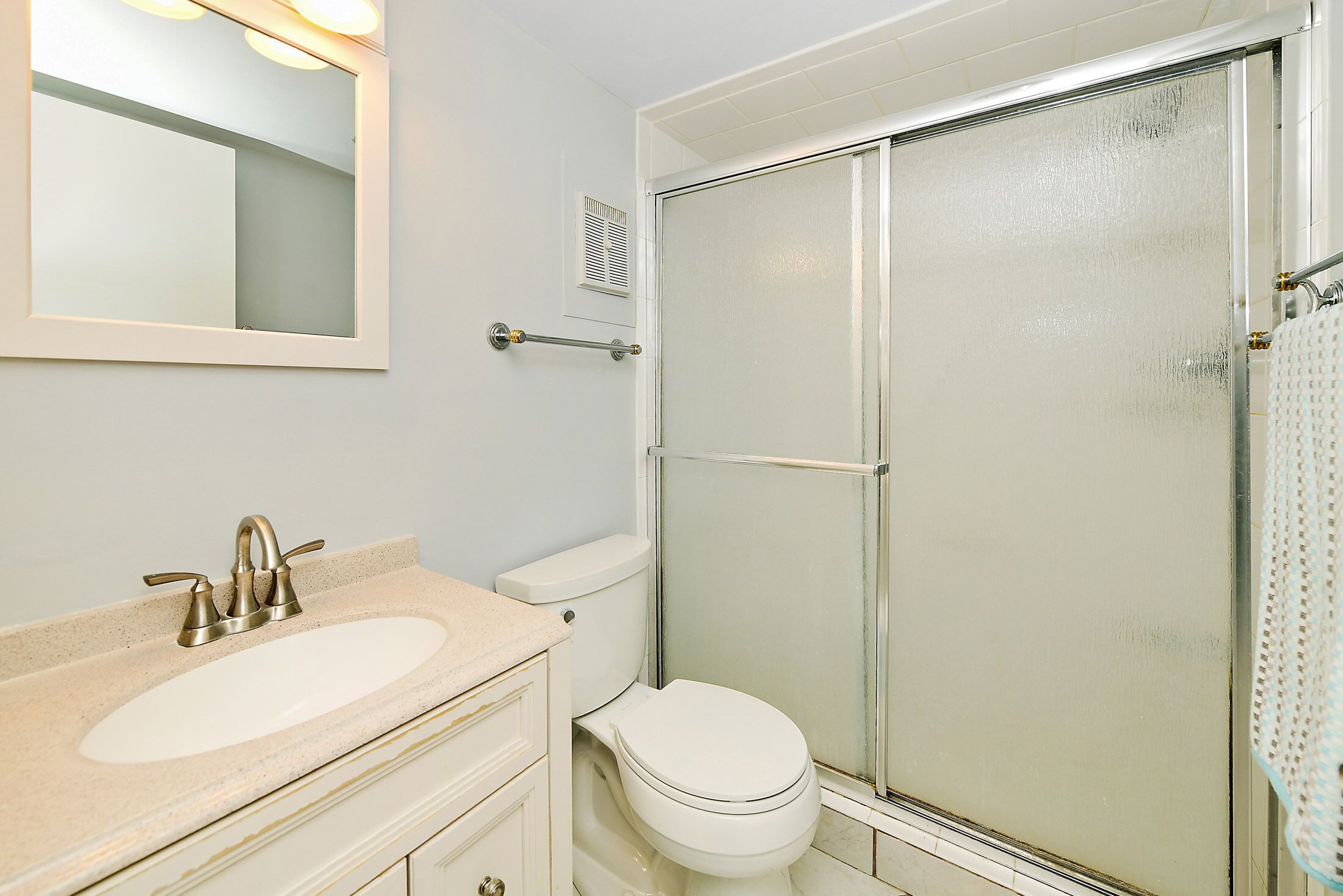 Baño con lavamanos, inodoro y ducha con mampara de vidrio.