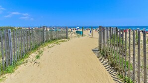 Un sendero arenoso que lleva a una playa, flanqueado por una valla de madera a ambos lados.