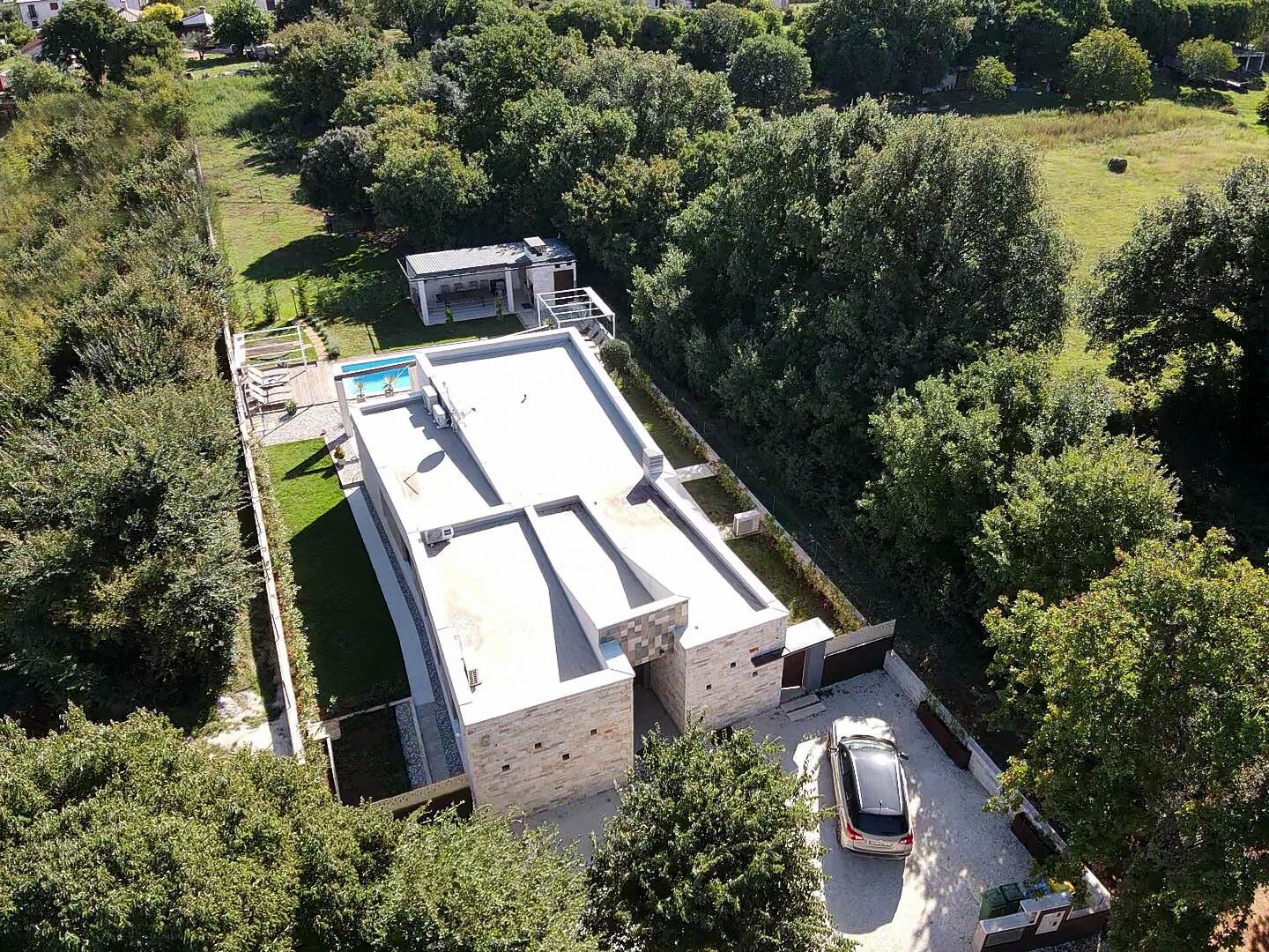 An aerial view of a modern house with a flat roof, a swimming pool, and a car parked in the driveway.