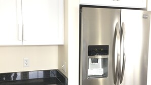 Ein Edelstahl-Kühlschrank mit Wasserspender, weiße Schränke und eine schwarze Arbeitsplatte.
