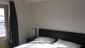 Ein Hotelzimmer mit Bett, Nachttisch, Lampe und einem Fenster mit Vorhängen.